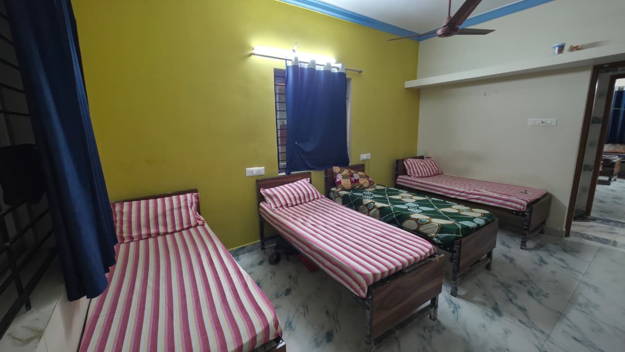 Four sharing room seen from the window, with four beds and a long shelf along the wall